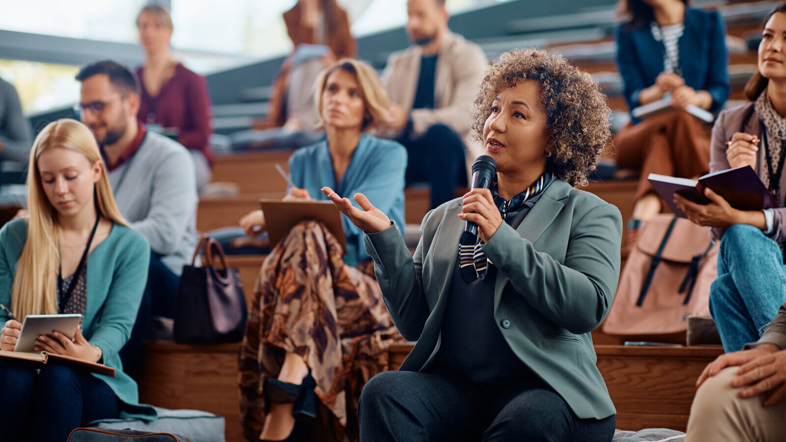 Woman holding a microphone and speaking from the audience at a public event