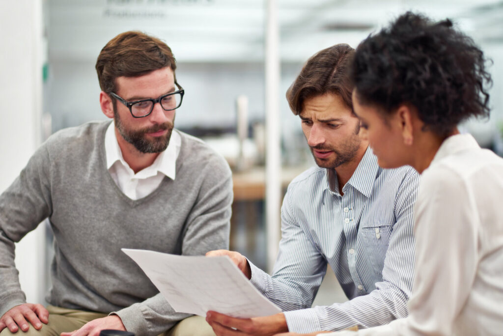 Three colleagues reading and discussing a printed document together