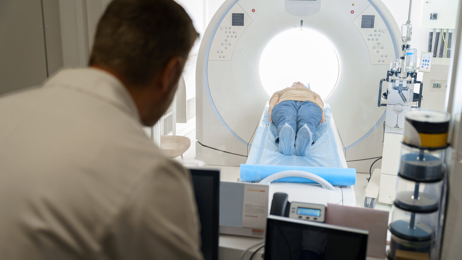 Technologist in a control room watching a patient lying in a CT scanner