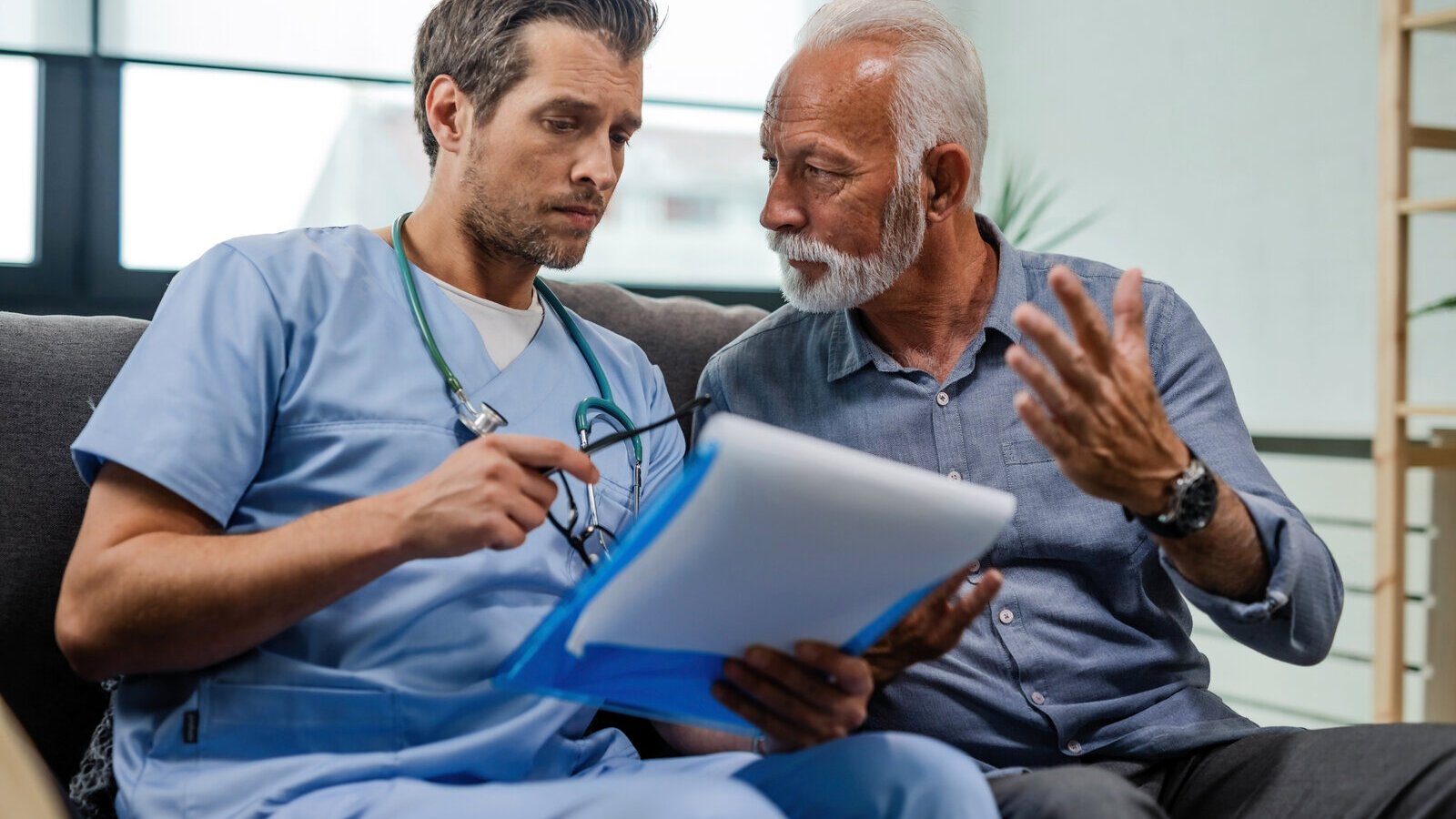 Doctor in scrubs going over papers in a folder with an older man seated beside him