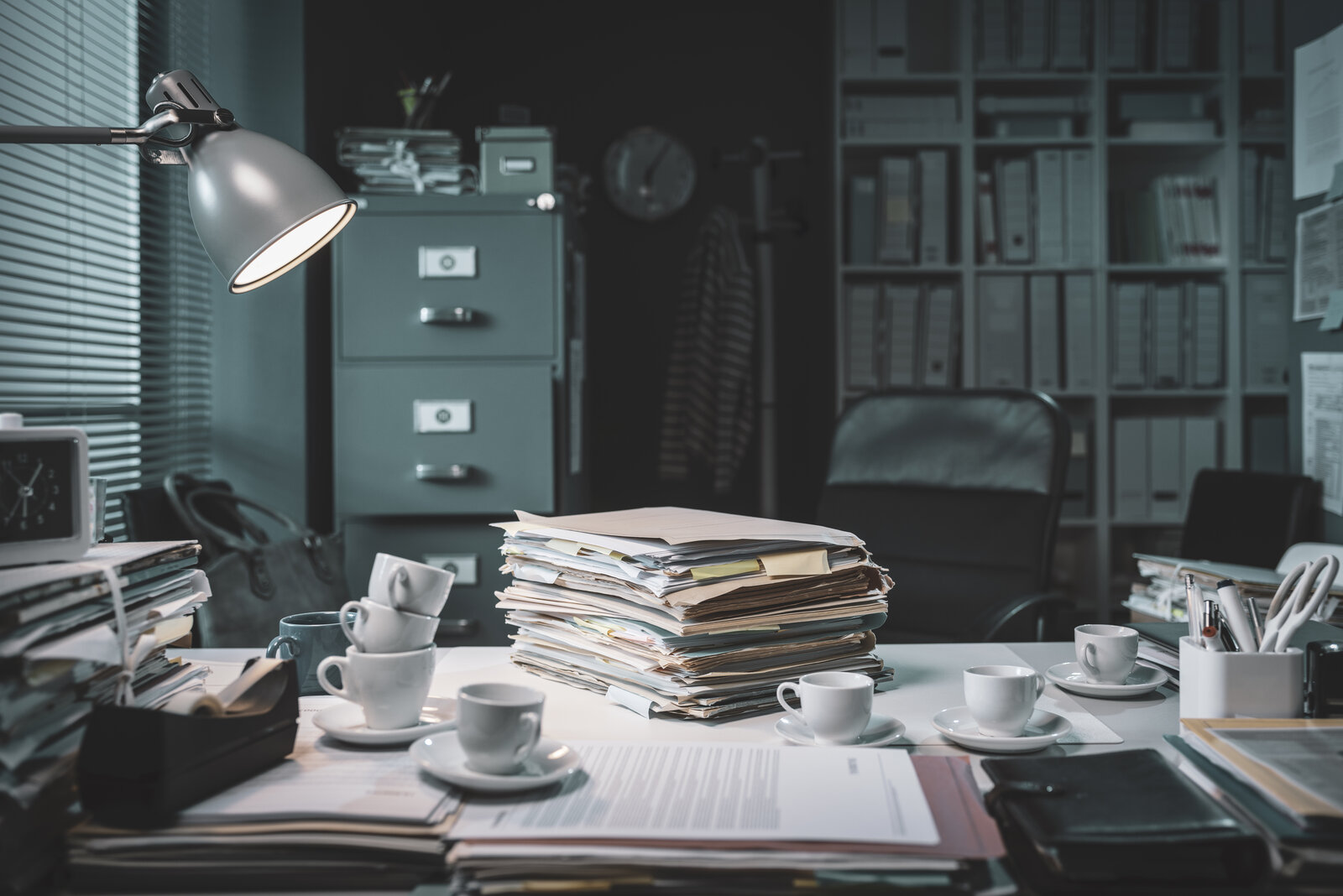 Empty office desk piled with stacks of papers and folders