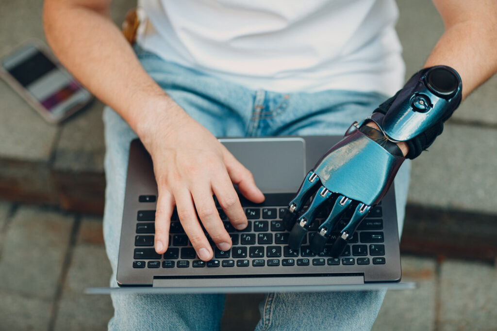 A human hand and a robotic hand typing on the same laptop