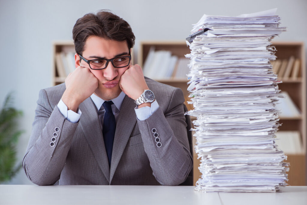 Pressure to publish Office worker with his head in his hands next to a tall stack of papers