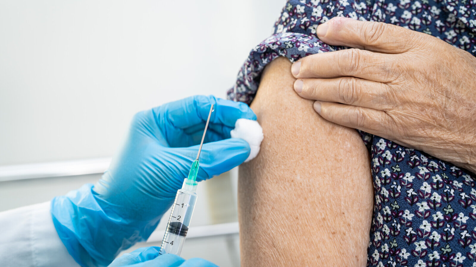 Health worker in blue gloves giving an injection in the upper arm of an older woman