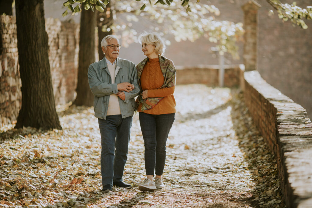 Older couple walking arm in arm along a leafy park path in autumn