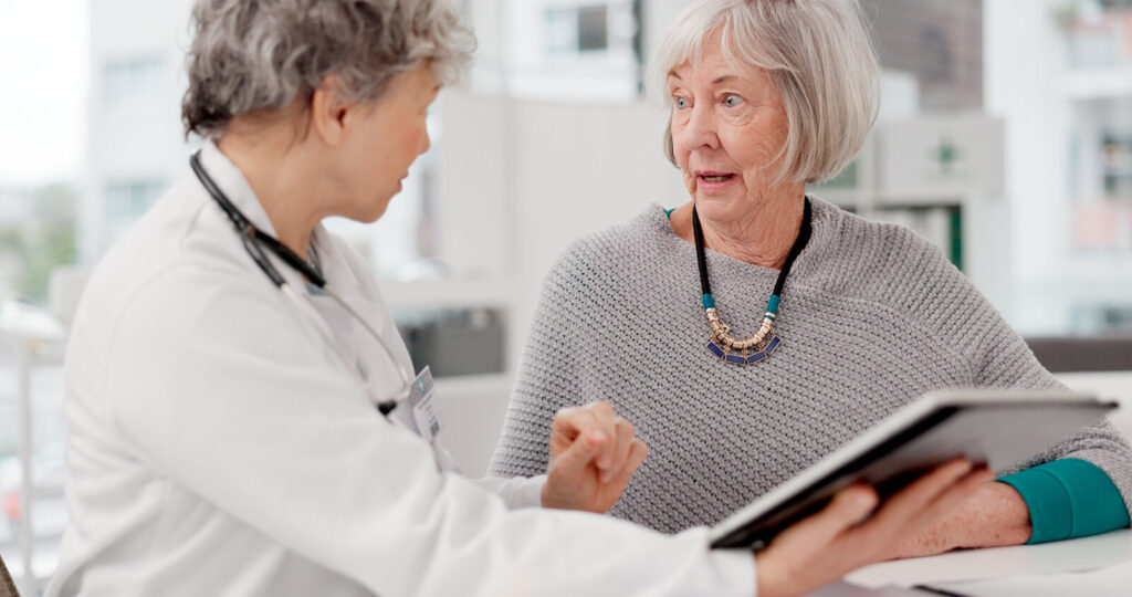 Older woman talking with a doctor who is holding a tablet