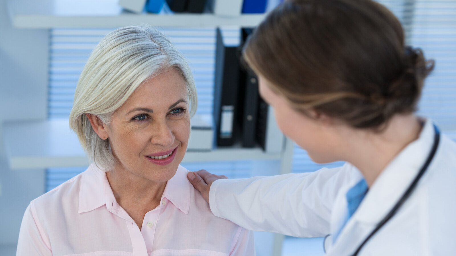 Older woman with gray hair smiling as a doctor rests a hand on her shoulder