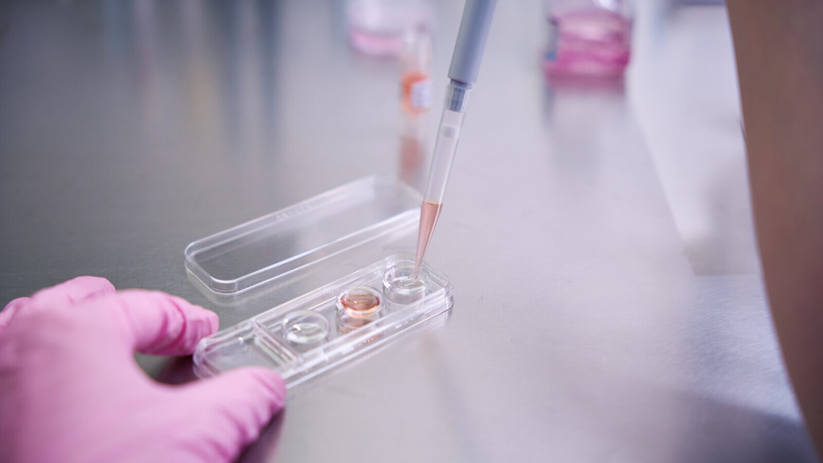 Gloved hand pipetting liquid into a small clear microfluidic chip