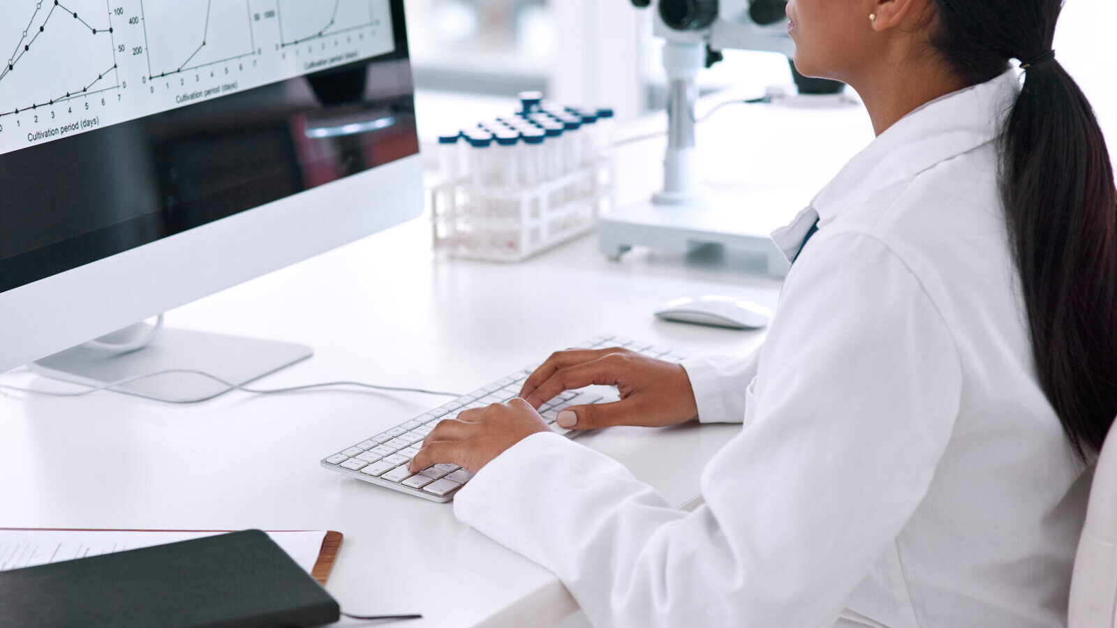 Researcher in a lab coat working at a computer showing data charts