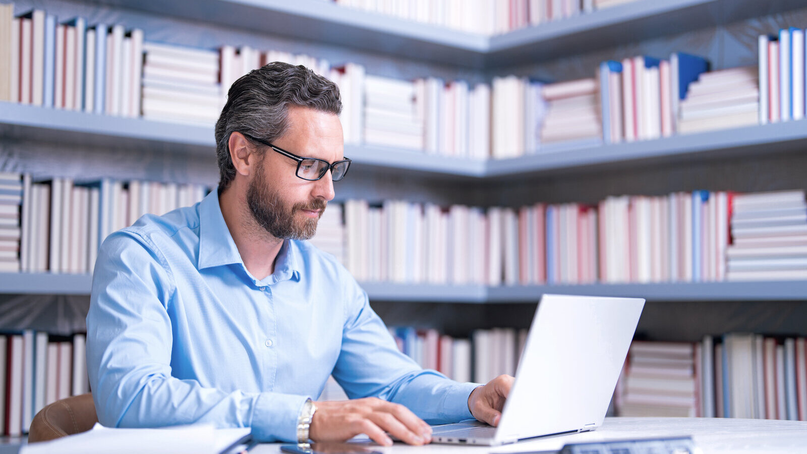 Researcher working on a laptop in a library surrounded by bookshelves