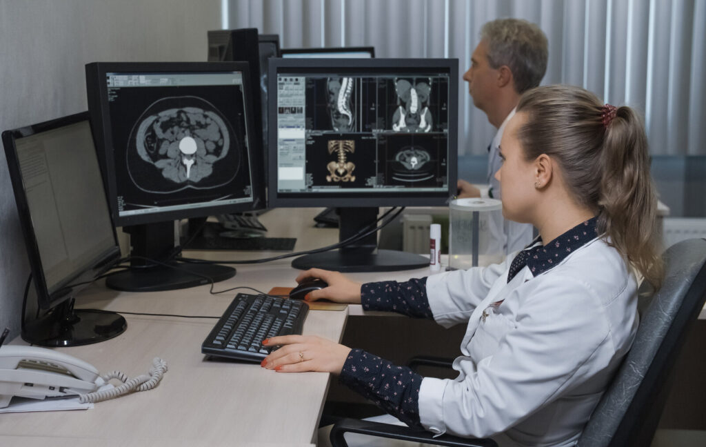 Clinicians at computer monitors reviewing cross-sectional CT images