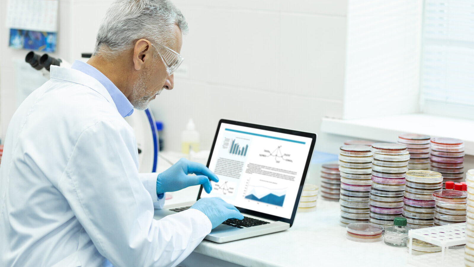 Scientist in a lab looking at charts on a laptop screen