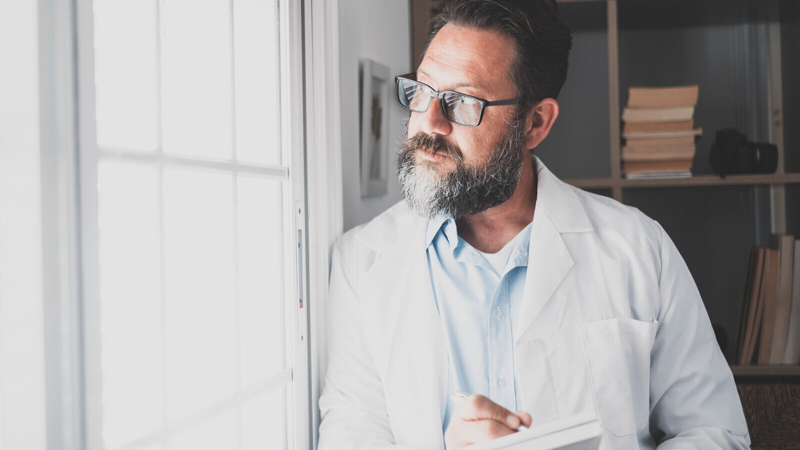 Scientist in a lab coat looking thoughtfully out of an office window