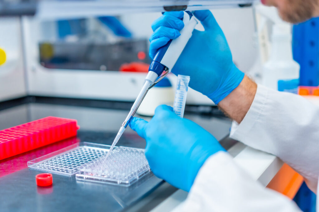 Gloved hands pipetting samples into a multi-well plate in a laboratory