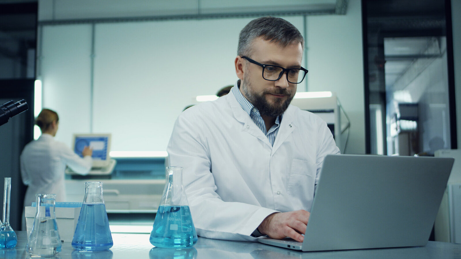 Scientist in a lab coat reading on a laptop at a laboratory bench
