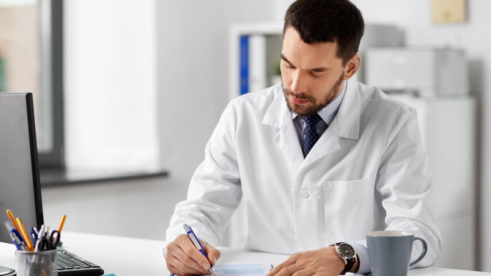 Scientist in a lab coat writing and signing a document at a desk