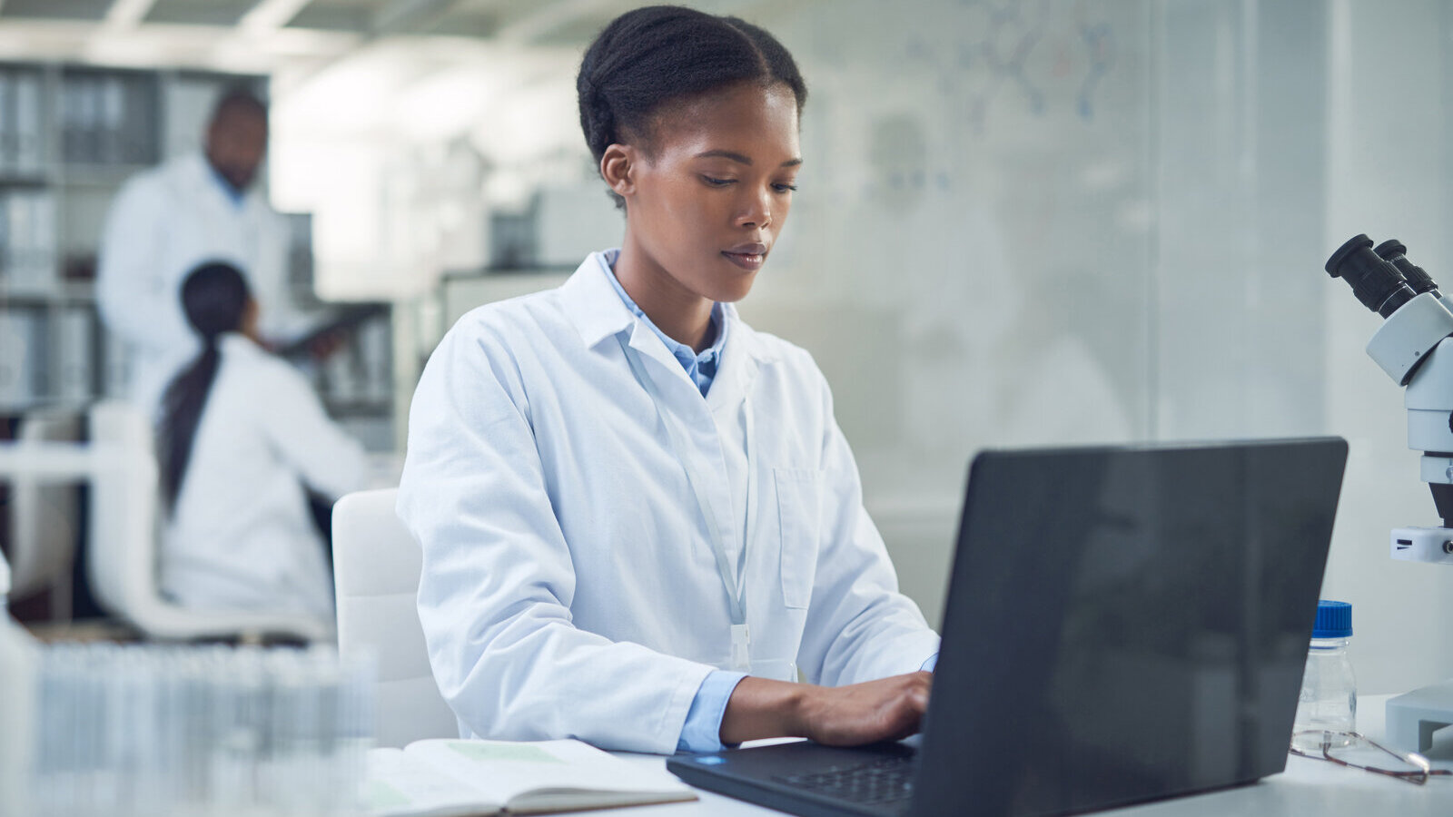 Scientist in a lab coat typing on a laptop at a laboratory desk