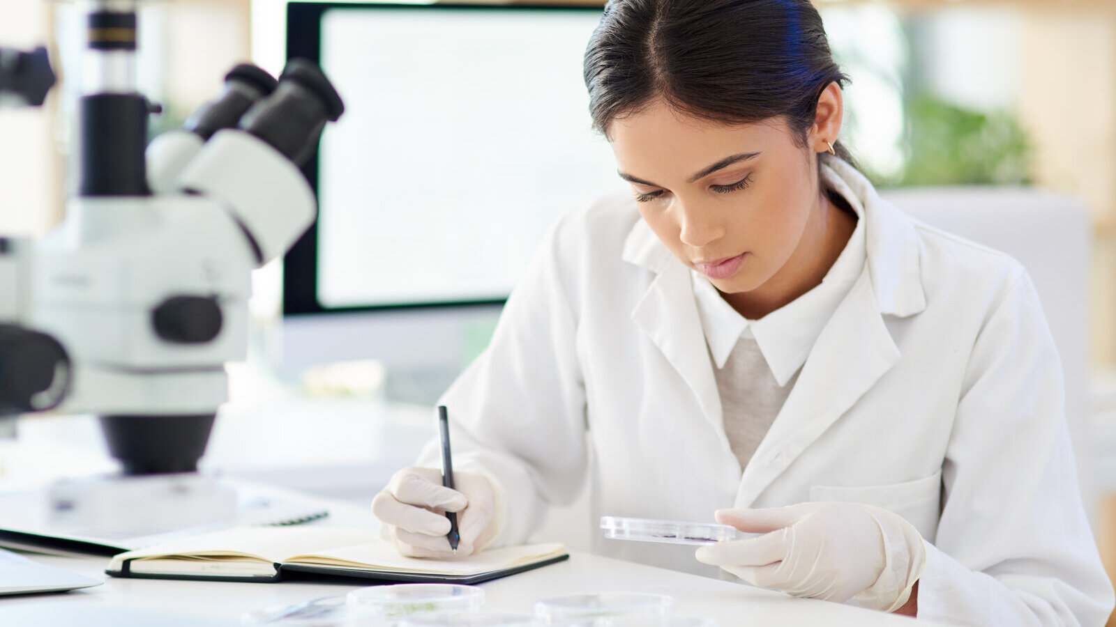 Scientist in a lab coat writing notes at a laboratory bench