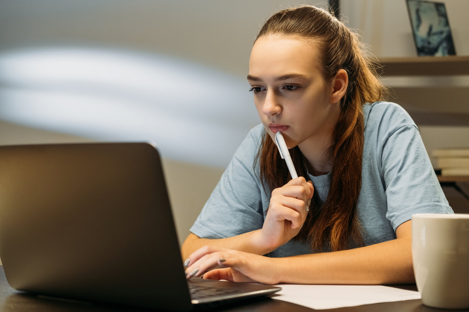 Student thinking with a pen in hand while writing on a laptop
