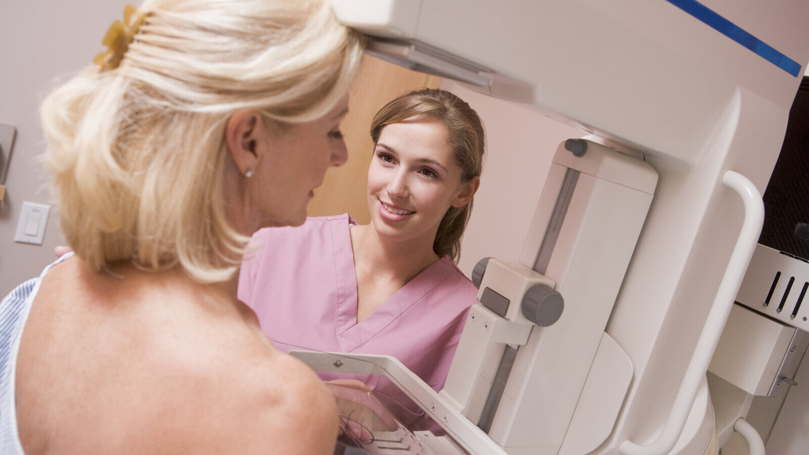 Middle-aged woman having a mammogram while a technologist adjusts the machine