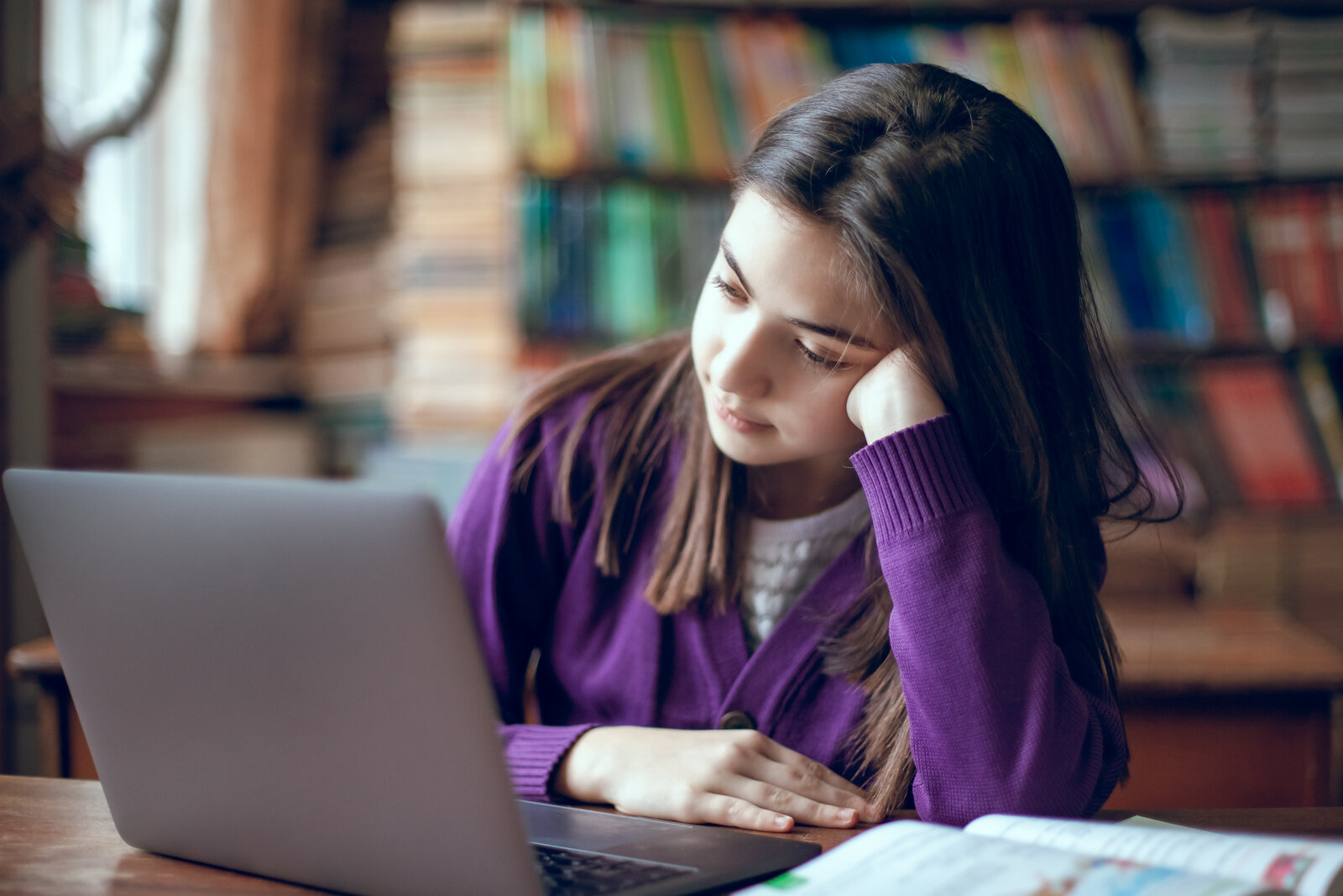 Worried student resting her head on her hand while looking at a laptop in a library