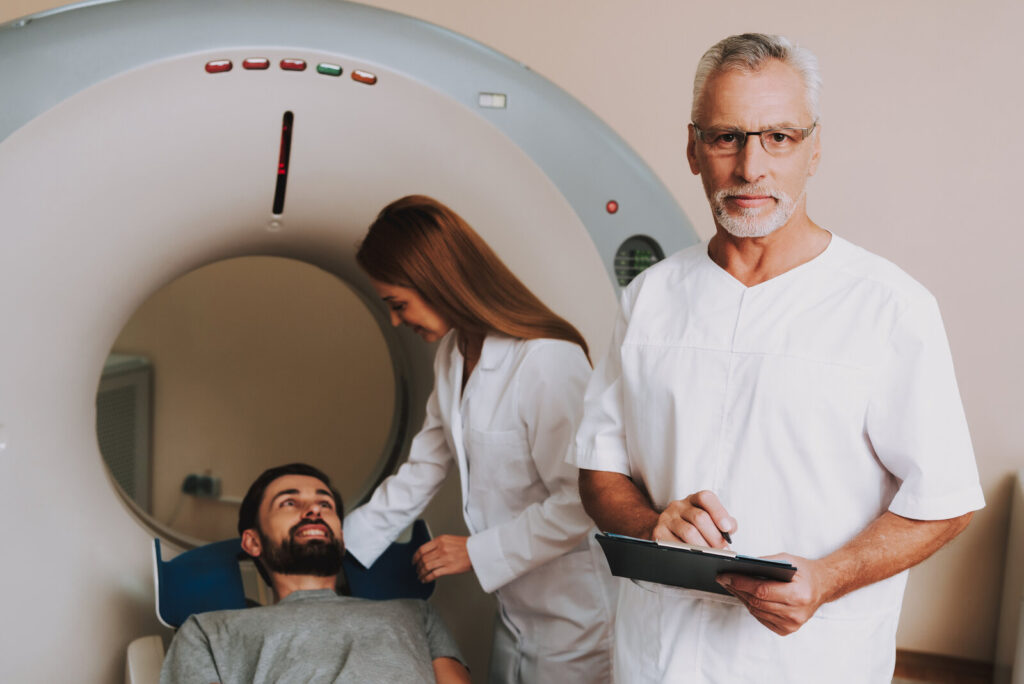 Patient lying on a CT scanner table while two clinicians prepare the scan