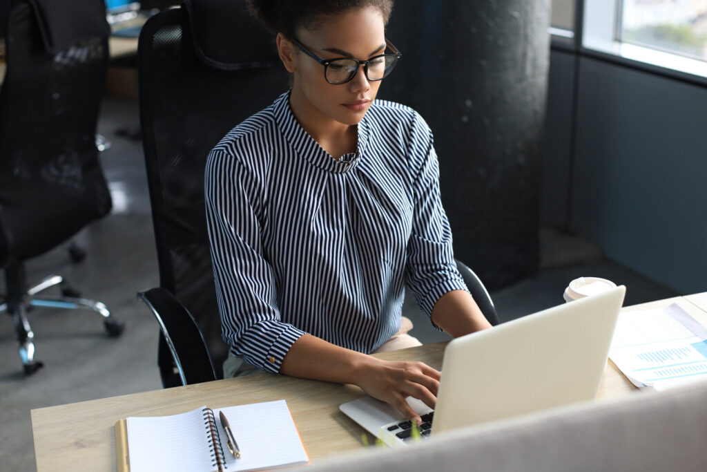 Researcher in glasses working on a laptop at an office desk with a notebook